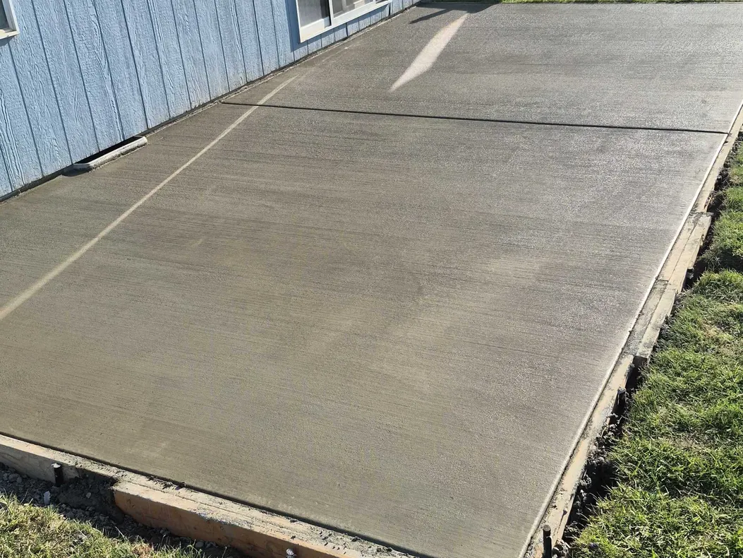 New concrete slab with the wood forms still in place against a blue house, building pads