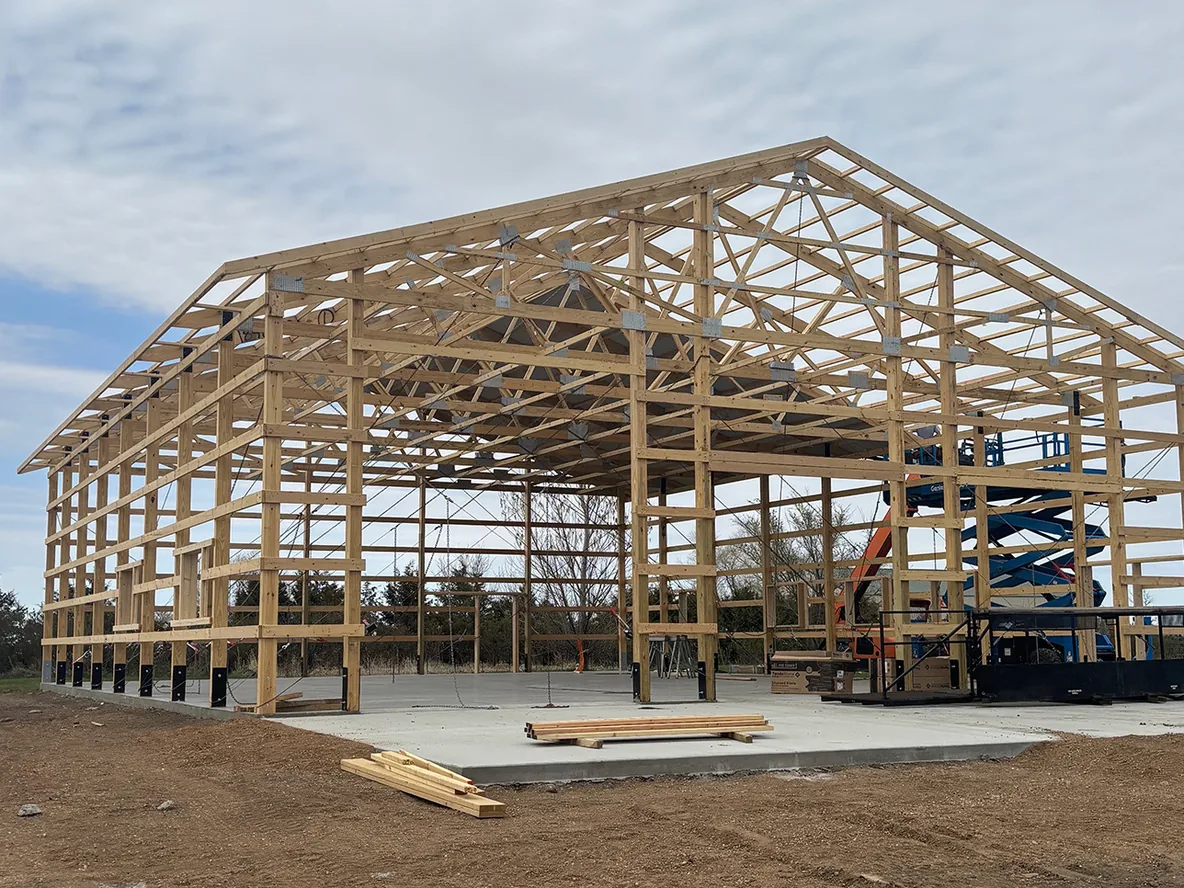 New concrete slab with a wood post frame shop being framed on it, building pads