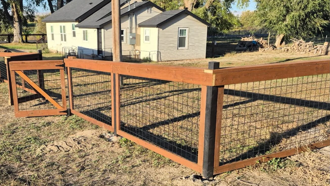 Wood frame fence with wire panels and a gate beside a house, general contracting