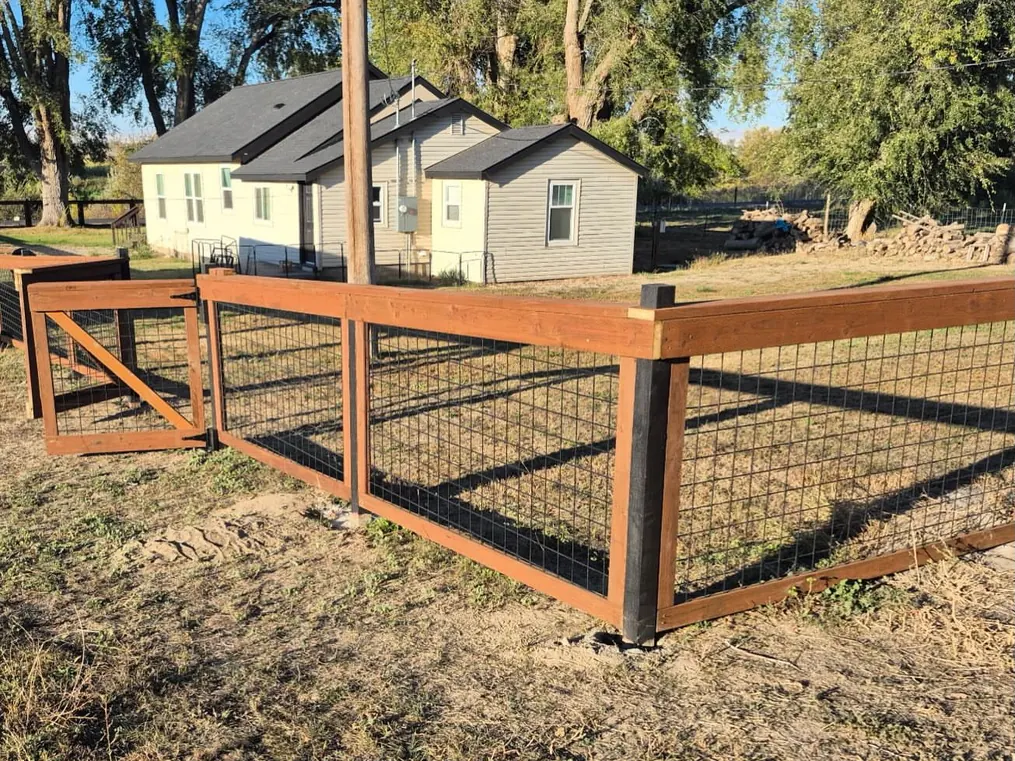 Wood frame fence with wire panels and a gate in front of a house, general contracting