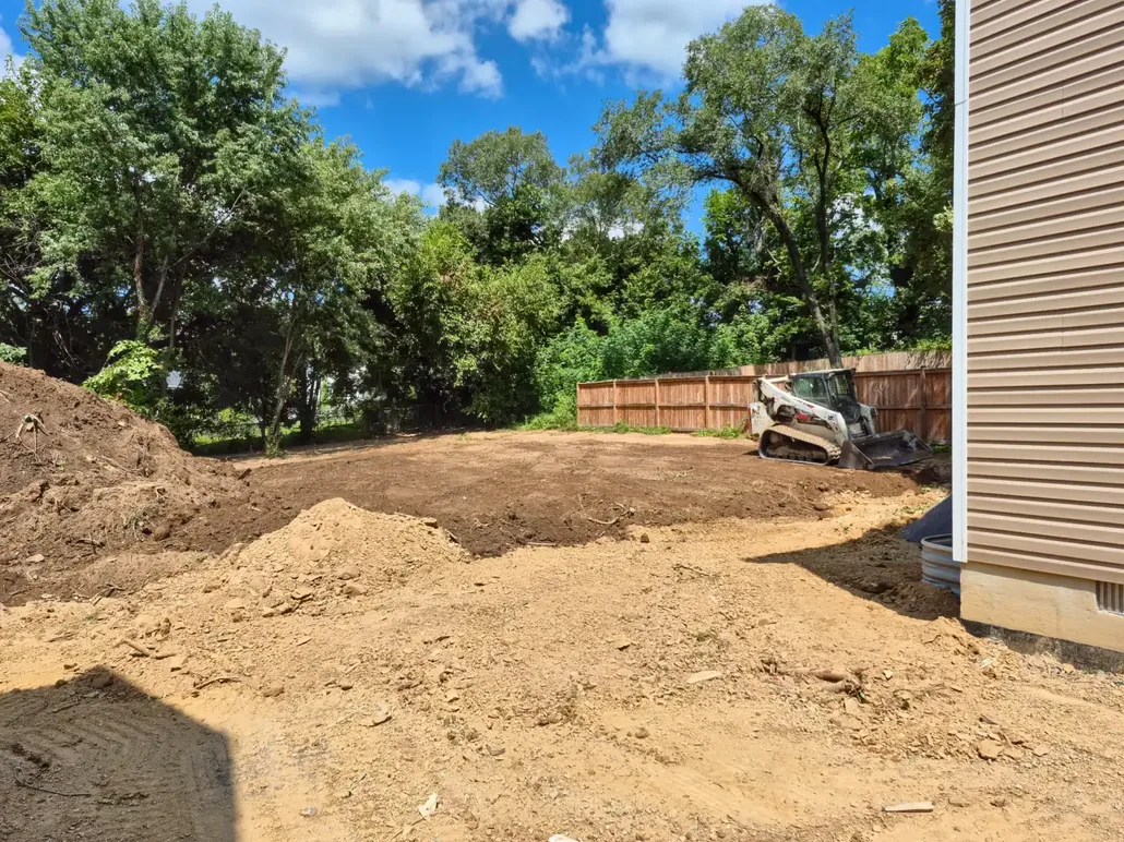 Freshly graded dirt backyard with a compact track loader by a wood fence, grading