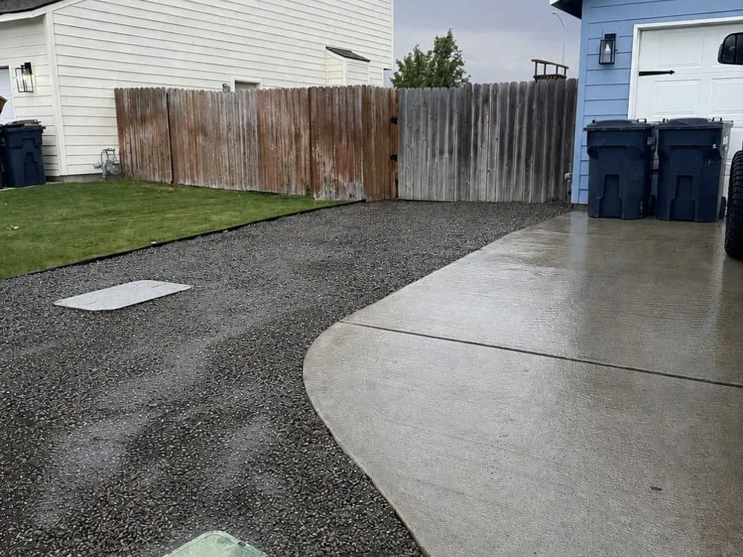 Finished gravel parking pad beside a concrete driveway and a wood fence, grading