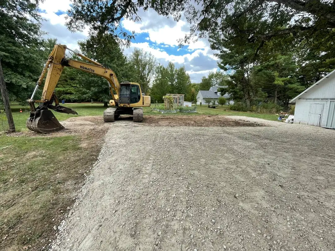 Freshly spread and compacted gravel pad on a rural lot with a tracked excavator, site preparation