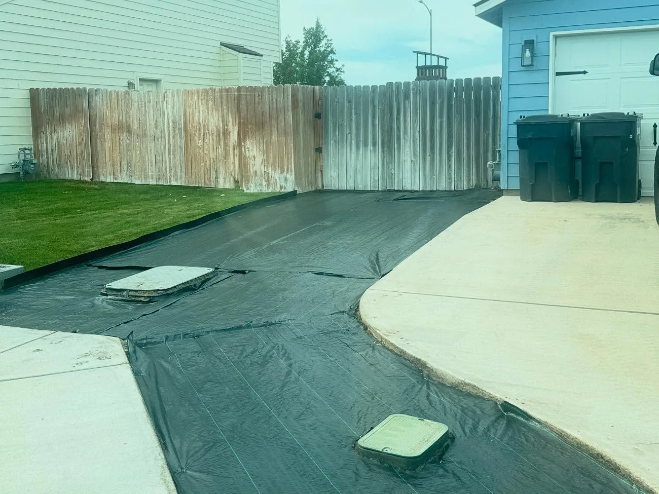 Stripped and leveled ground covered with black landscape fabric beside a driveway, site preparation